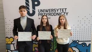 Trzej uczniowie na tle banneru Uniwersytetu Przyrodniczego w Lublinie z certyfikatami uczestnictwa