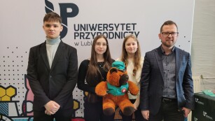 Trzej uczniowie wraz z opiekunem na tle banneru Uniwersytetu Przyrodniczego w Lublinie