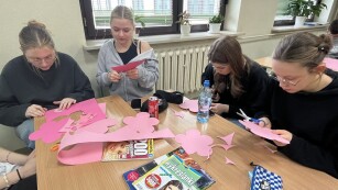 Uczniowie w sali lekcyjnej wycinają kwiaty z różowego papieru