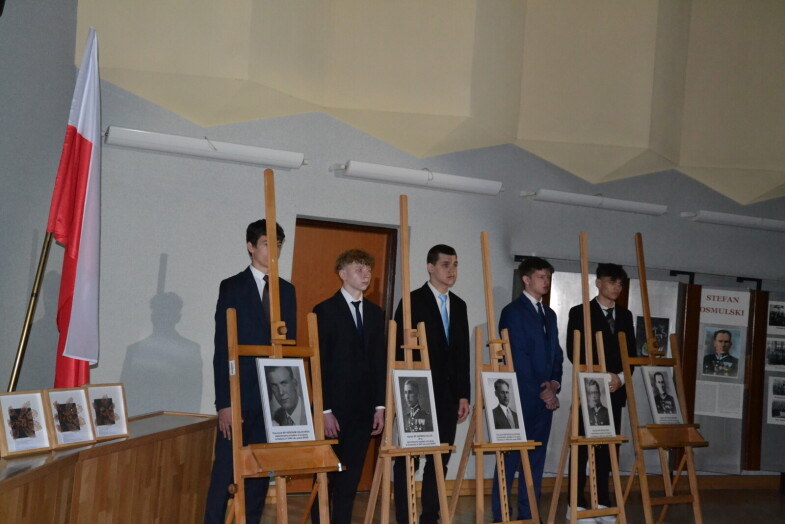 pięciu uczniów stoi przy portretach poległych oficerów