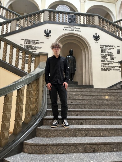 Uczeń stoi w holu Akademii Górniczo-Hutniczej w Krakowie, na schodach przed pomnikiem Stanisława Staszica, patrona uczelni,