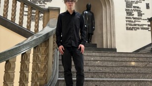 Uczeń stoi w holu Akademii Górniczo-Hutniczej w Krakowie, na schodach przed pomnikiem Stanisława Staszica, patrona uczelni,