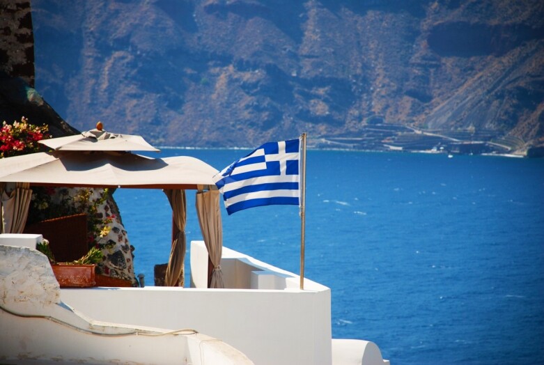 Widok krajobrazu w Grecji - morze i biały dom z niebieskimi dachami i flaga Grecji