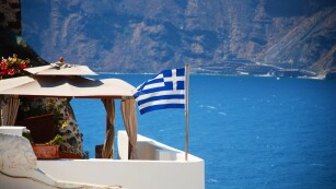 Widok krajobrazu w Grecji - morze i biały dom z niebieskimi dachami i flaga Grecji